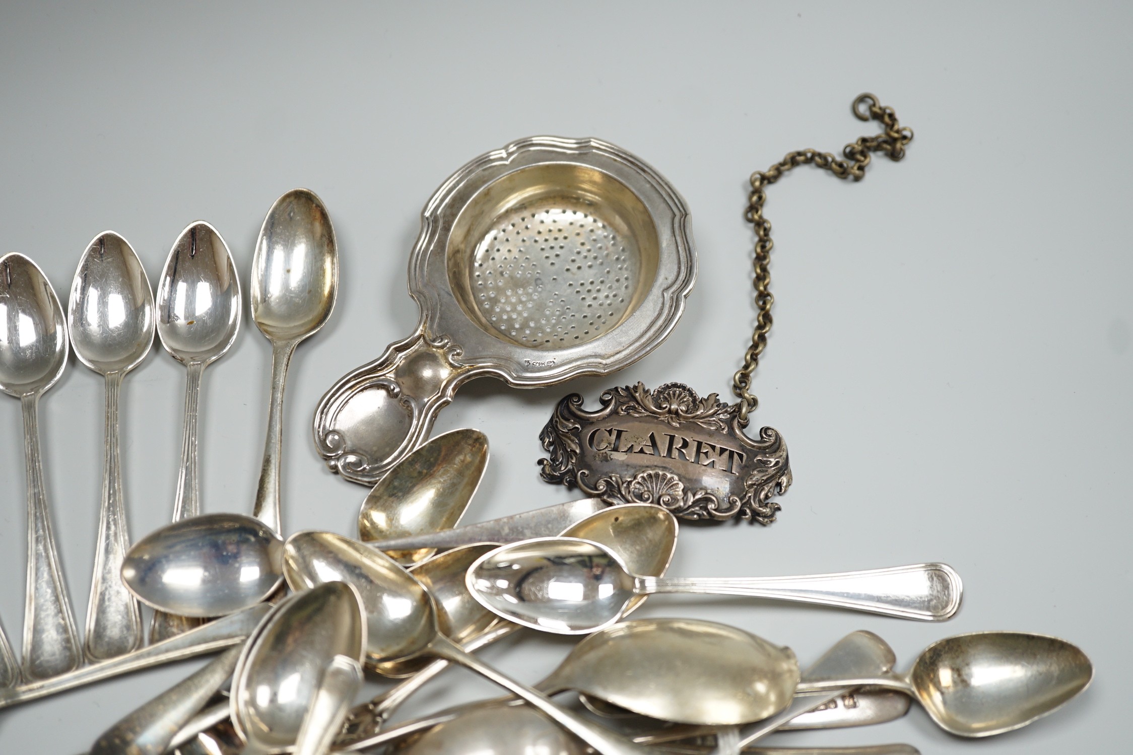 A group of mixed silver and white metal items including flatware, Dutch fish slice, German 800 tea strainer, George IV 'Claret' wine label, etc. and a plated spoon.